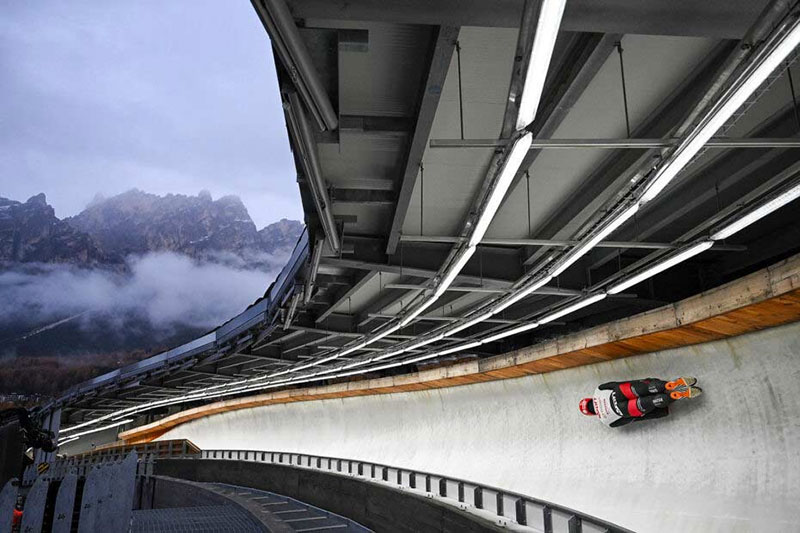 Pista olimpică „Eugenio Monti” din Cortina d’Ampezzo, reconstruită pentru Jocurile din 2026, îmbină structura de oțel (ascunsă sub canalul de gheață) cu elemente de integrare protejat anticoroziv prin zincare termică în peisajul montan.